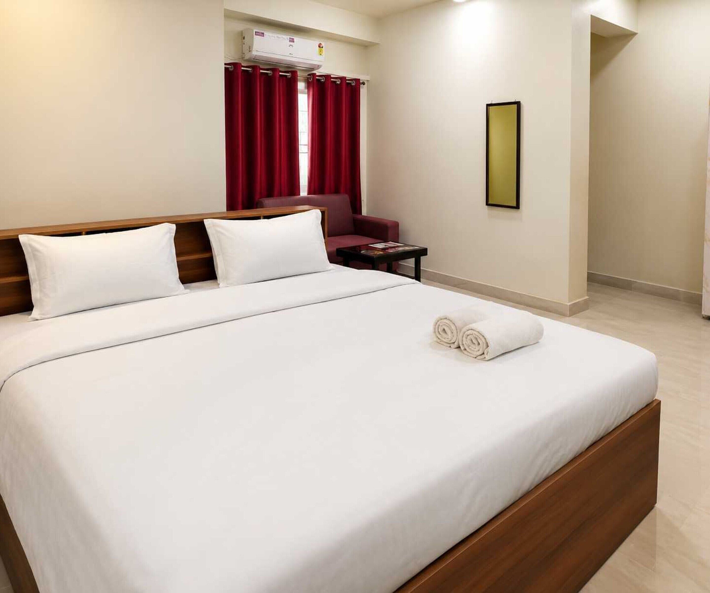 A hotel room with a large bed, a chair, a small table, a wall-mounted air conditioner, and a framed picture.