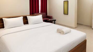 A hotel room with a large bed, a chair, a small table, a wall-mounted air conditioner, and a framed picture.