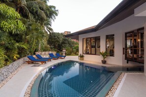 A swimming pool with lounge chairs, surrounded by a stone wall and lush greenery. - Surin Lake Villa (Thalang District)