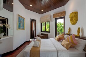 A hotel room with a large bed, a wooden headboard, a window with a view of greenery, a wall-mounted sculpture, and a framed picture. - Surin Lake Villa (Thalang District)