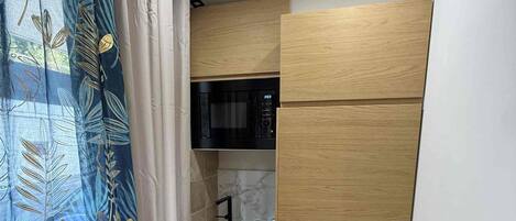 A compact room with a kitchenette, a bed, and a curtain with a leaf pattern.