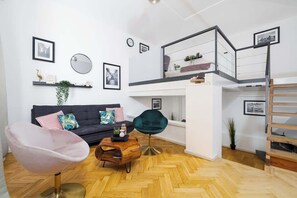A modern living room with a sofa, a round mirror, and a staircase leading to an upper level. - Large Central Apt | Game Room • Xbox Pass • Fun (Praha 2)