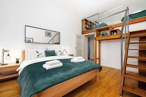 A bedroom with a bunk bed, a bedside table with a lamp, a framed picture on the wall, and a green bedspread. - Large Central Apt | Game Room • Xbox Pass • Fun (Praha 2)