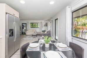Een moderne keuken met een inbouwkoelkast, een eethoek met een ronde tafel gedekt voor vier personen, en een woonkamer met een bank en salontafel.