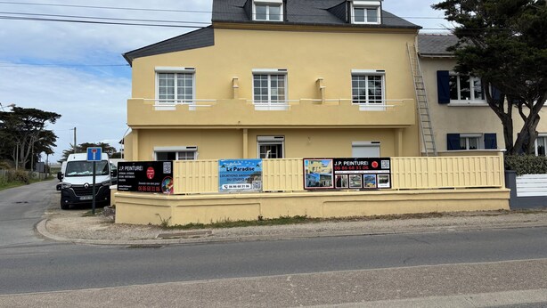 Un edificio de dos pisos con fachada amarilla, múltiples ventanas y un cartel anunciando un negocio.