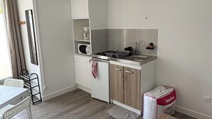 Una cocina compacta con armarios blancos, un microondas y un lavamanos. Hay una pequeña zona de comedor con una mesa y sillas.