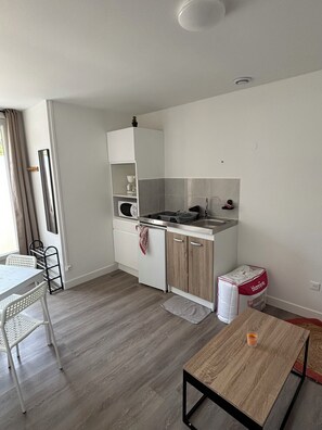 A compact kitchen with white cabinets, a microwave, and a sink. There's a small dining area with a table and chairs. - Between Land and Sea (Batz-sur-Mer)