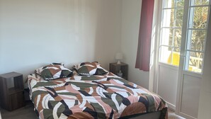 Un dormitorio con cama, mesita de noche, lámpara y ventana con cortinas.