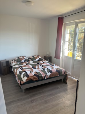 A bedroom with a bed, a nightstand, a lamp, and a window with curtains. - Between Land and Sea (Batz-sur-Mer)
