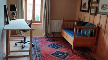 Une pièce avec un lit en bois, un bureau avec une chaise, une fenêtre avec des rideaux et un tapis à motifs.