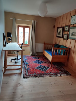 A room with a wooden bed, a desk with a chair, a window with curtains, and a patterned rug. - Vacation home, peaceful and surrounded by nature, sleeps 6/8/10, Haute-Loire—Tiranges, (Tiranges)