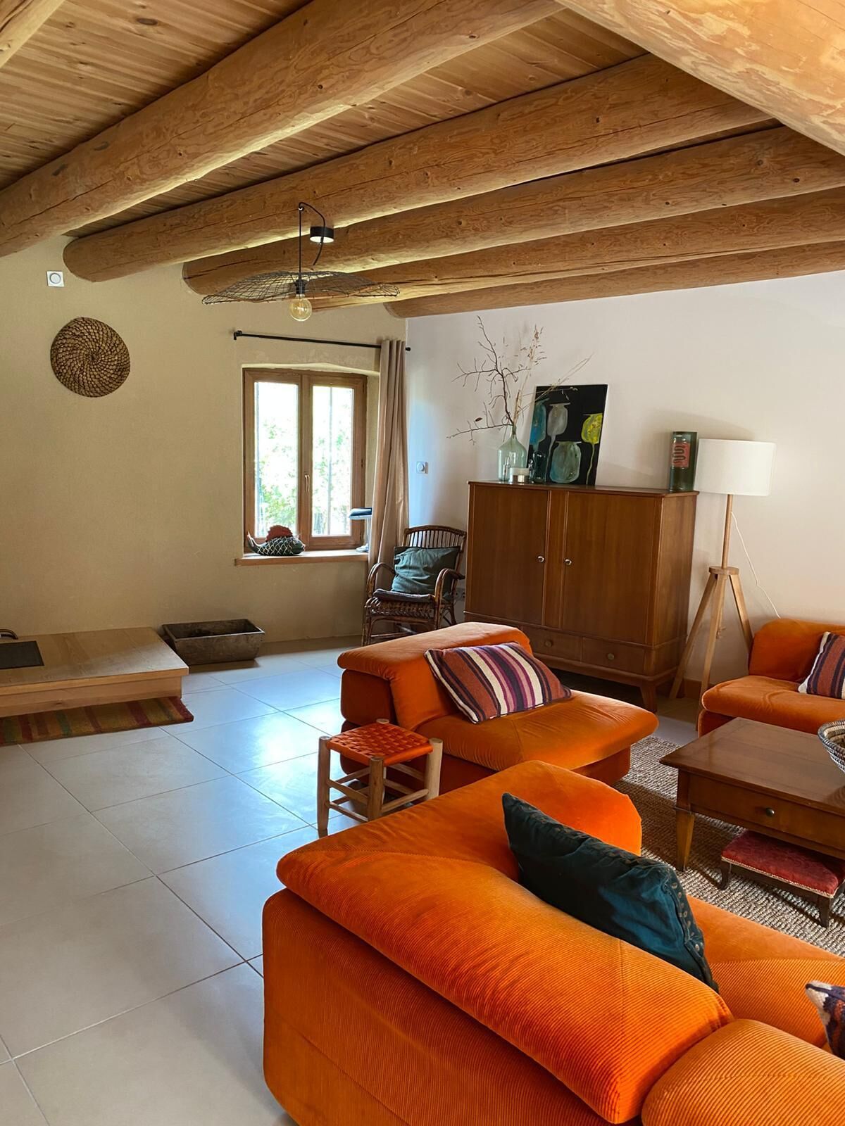 Een woonkamer met een hoog houten plafond, een zithoek, een houten kast en een vloerlamp.