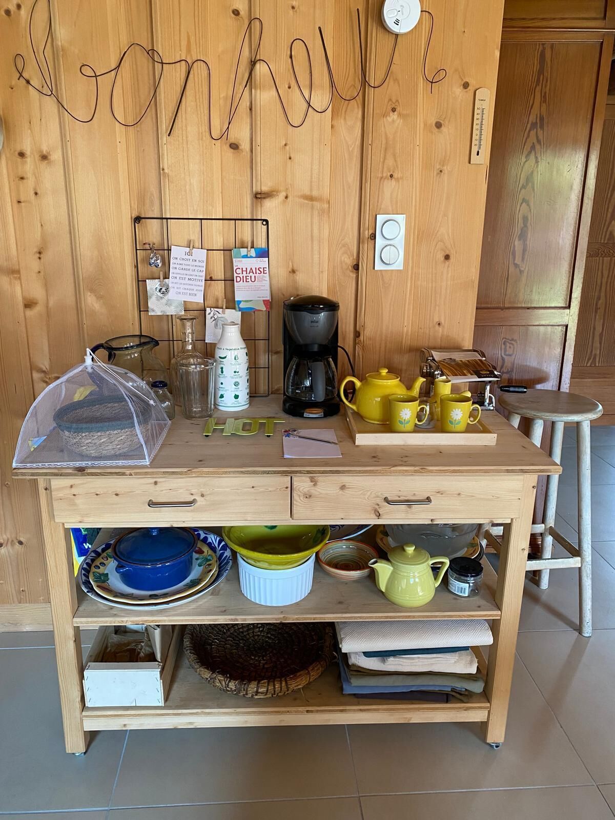 Une table en bois, avec des ustensiles de cuisine, une machine à café et une pancarte avec du texte en français.