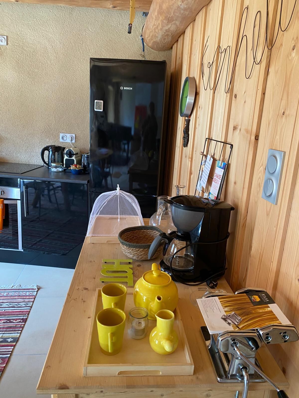 Un coin cuisine équipé d’une machine à café, d’une bouilloire et d’ustensiles de cuisine, le tout posé sur un plan de travail en bois.
