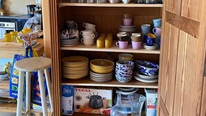 A wooden cabinet with shelves containing glassware, plates, and kitchen utensils.