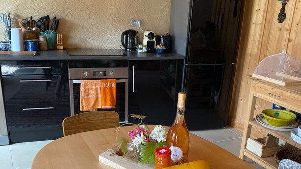 A kitchen with a wooden table, a bottle, a yellow squash, and a vase with flowers.