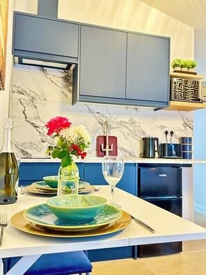 A modern kitchen with marble countertops, a built-in oven, and a dining area with a table set for two. - Modern Self-Contained Studio Annexe with Kitchenette and Private Entrance (Oxford)
