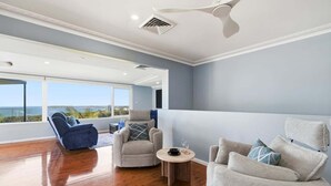 Ein geräumiges Wohnzimmer mit hoher Decke, einem Deckenventilator und Blick ins Freie.