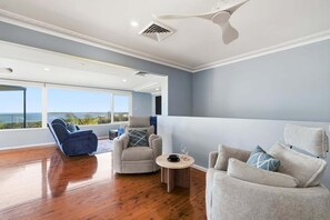 Ein geräumiges Wohnzimmer mit hoher Decke, einem Deckenventilator und Blick ins Freie.