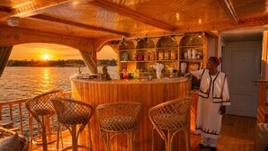 Angolo bar con sedie in vimini, soffitto in legno e vista sul tramonto sull'acqua.
