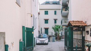 Una calle estrecha con un auto estacionado, un portón verde y un edificio con múltiples ventanas y balcones.