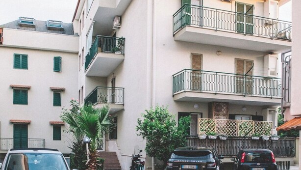 Un edificio residencial de varios pisos con balcones, coches estacionados y cielo despejado.