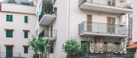 A multi-story residential building with balconies, parked cars, and a clear sky.