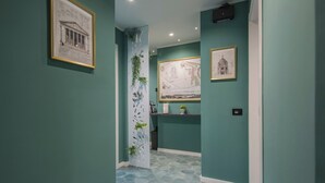 Un pasillo con paredes verde agua, un panel decorativo blanco con plantas y dibujos arquitectónicos enmarcados en las paredes.