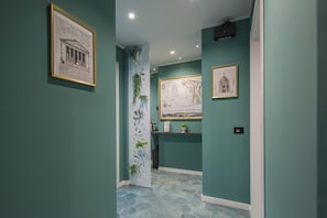 A hallway with teal walls, a white decorative panel with plants, and framed architectural drawings on the walls. - Gioia Home (Pompei)