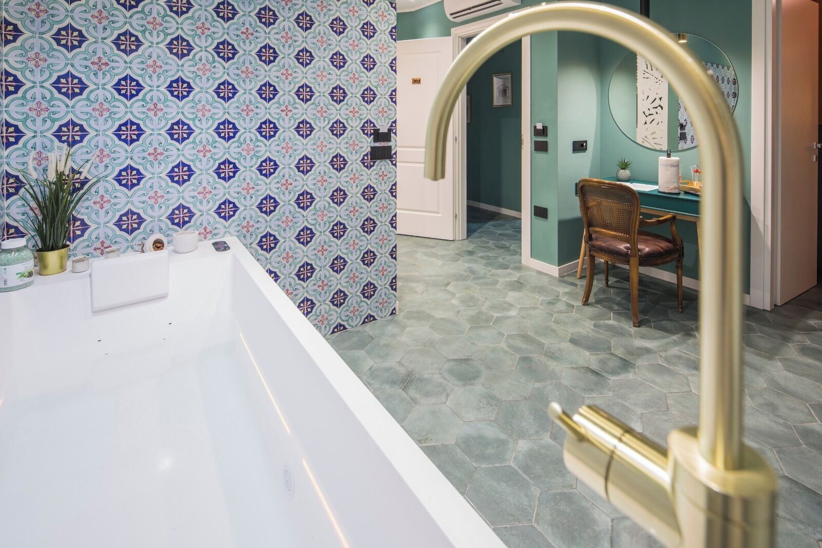 Un baño con bañera blanca, pared con diseño y baldosas hexagonales en el suelo.