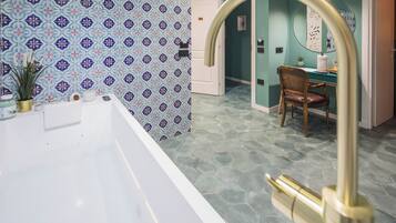 Un baño con bañera blanca, pared con diseño y baldosas hexagonales en el suelo.