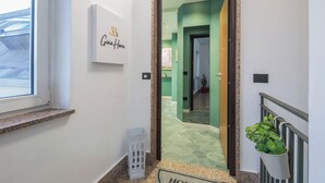 Un pasillo con un letrero que dice 'Giovita Home', una planta en maceta y una puerta que da a otra habitación.
