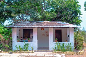 A small, single-story house with a tiled roof, a front porch, and potted plants.