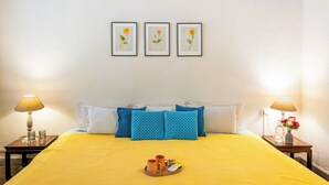 Una camera d'albergo con un letto, cuscini, un vassoio con oggetti e quadri appesi al muro.