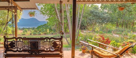 A wooden swing bench under a pergola with a view of a mountainous landscape.