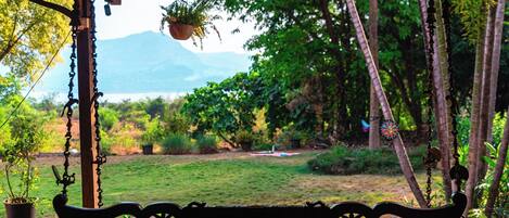 A wooden bench with intricate carvings, a hanging plant, and a view of a lush garden with a mountain in the distance.