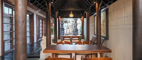 An indoor dining area with a wooden table and chairs, a hanging light fixture, and a view of the outside.