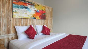 A hotel room with a large bed, white bedding, two red pillows, and a colorful abstract painting on the wooden headboard.