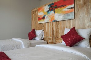 A hotel room with two beds, each with white bedding and red pillows, and a large abstract painting on the wooden headboard.