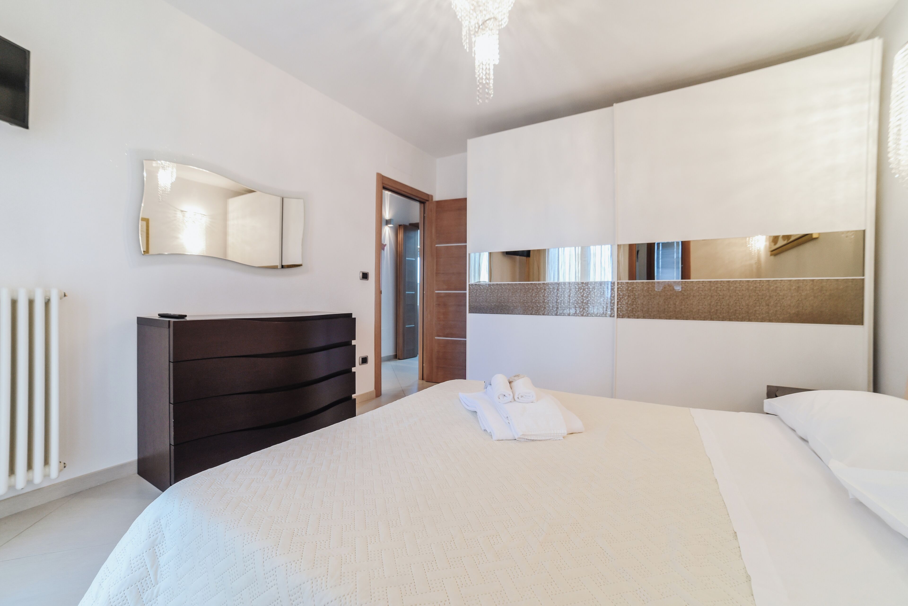 A hotel room with a large bed, a dark wooden dresser, a mirror, and a radiator.