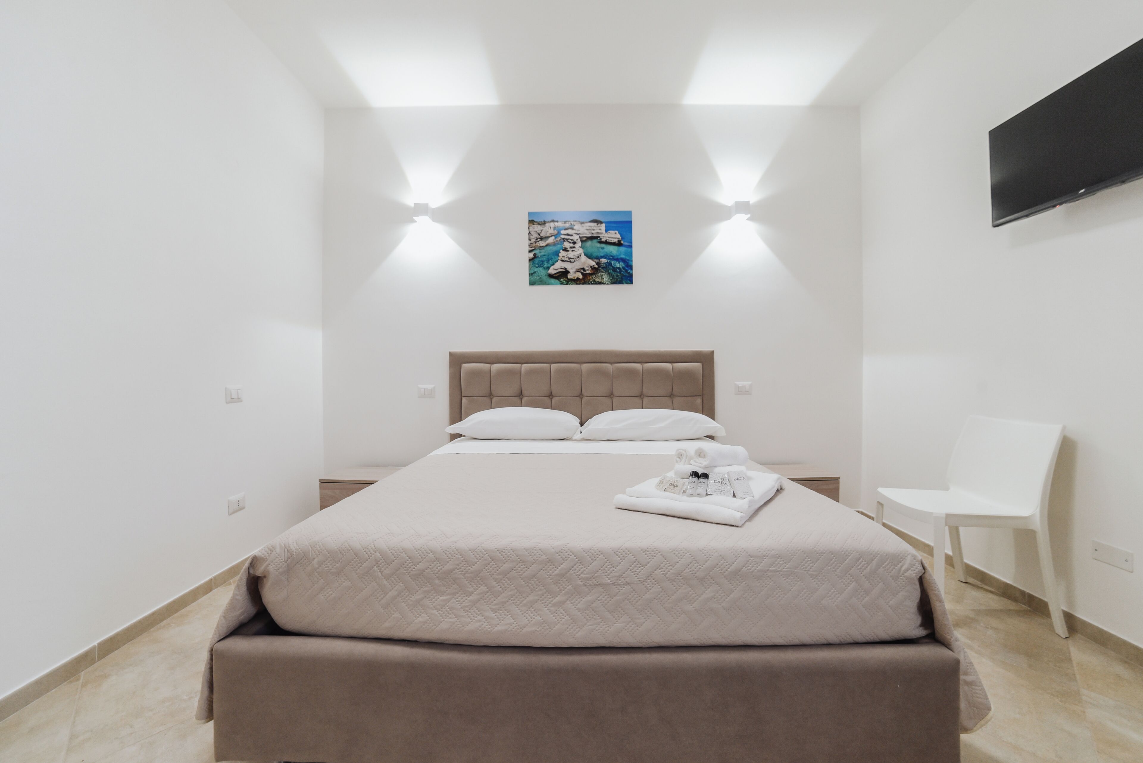 Une chambre à coucher au style minimaliste, avec un lit, une table de chevet, une chaise et un tableau accroché au mur.