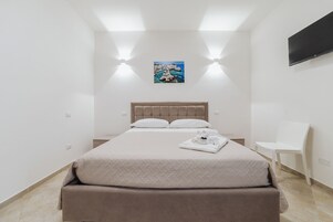 A minimalist bedroom with a bed, a bedside table, a chair, and a painting on the wall.