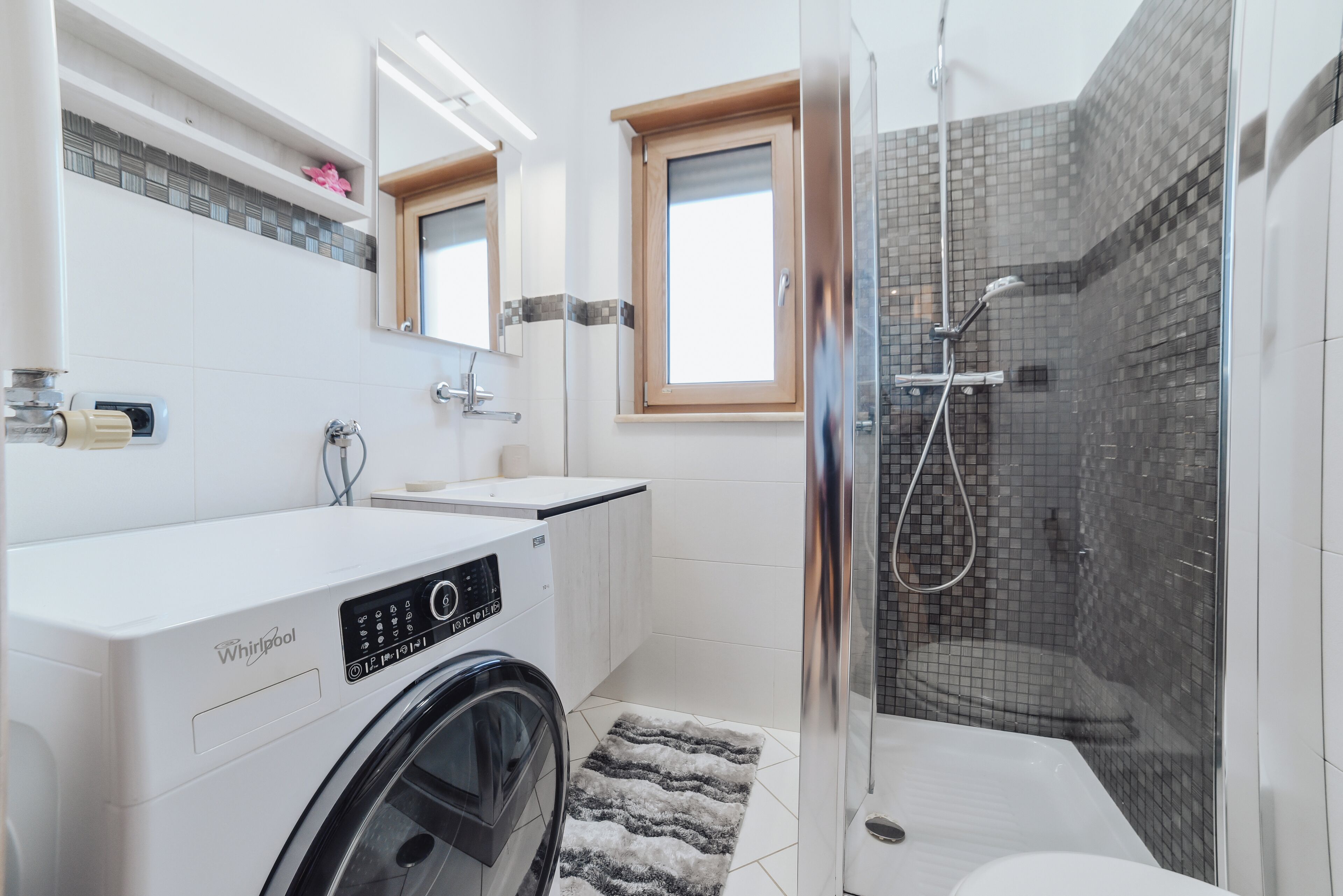 Un bagno moderno con lavatrice, cabina doccia in vetro e un water.