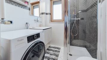 Un bagno moderno con lavatrice, cabina doccia in vetro e un water.