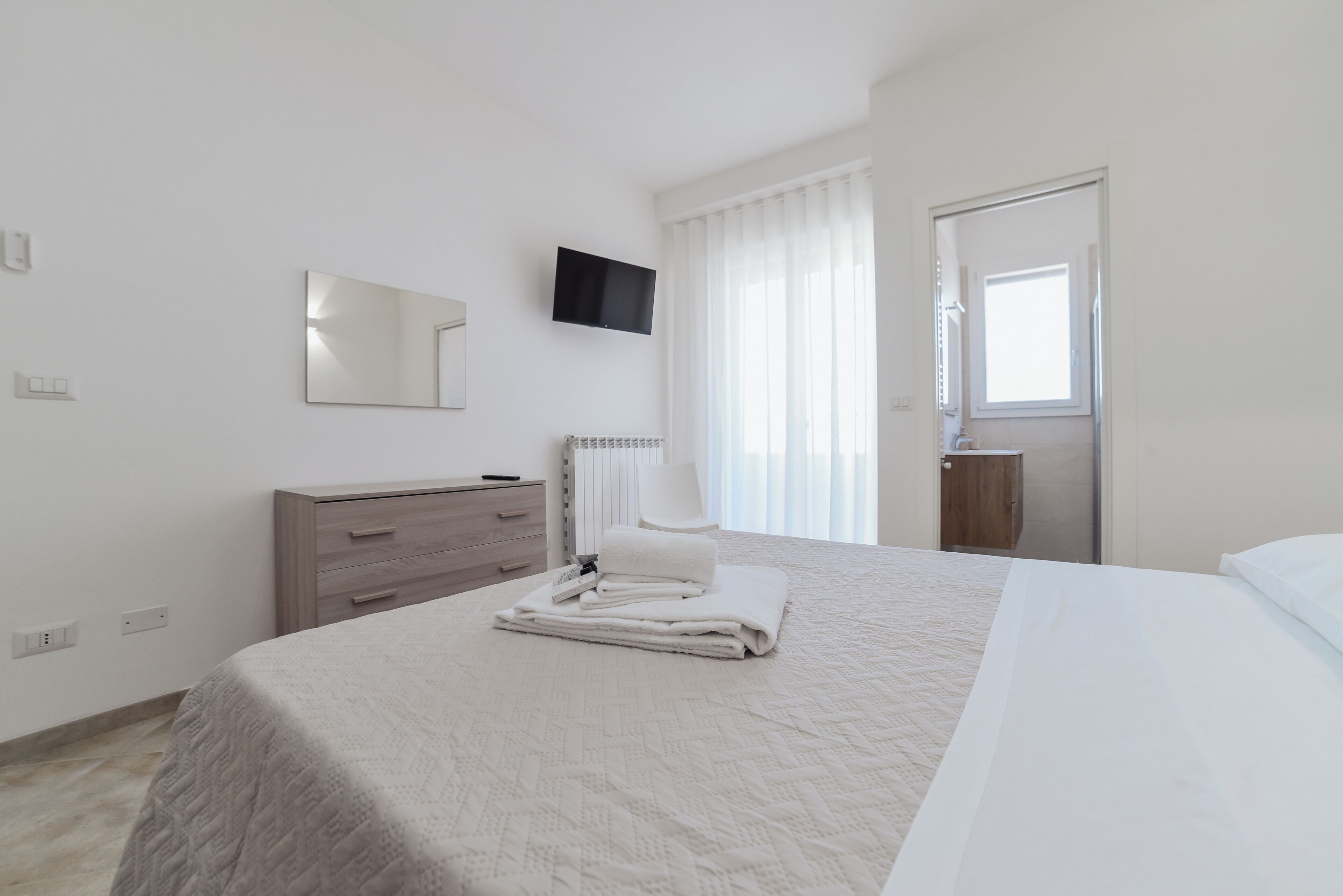 Ein Schlafzimmer mit einem Bett, einem Schminktisch, einem Spiegel, einem Fernseher und einem Fenster.