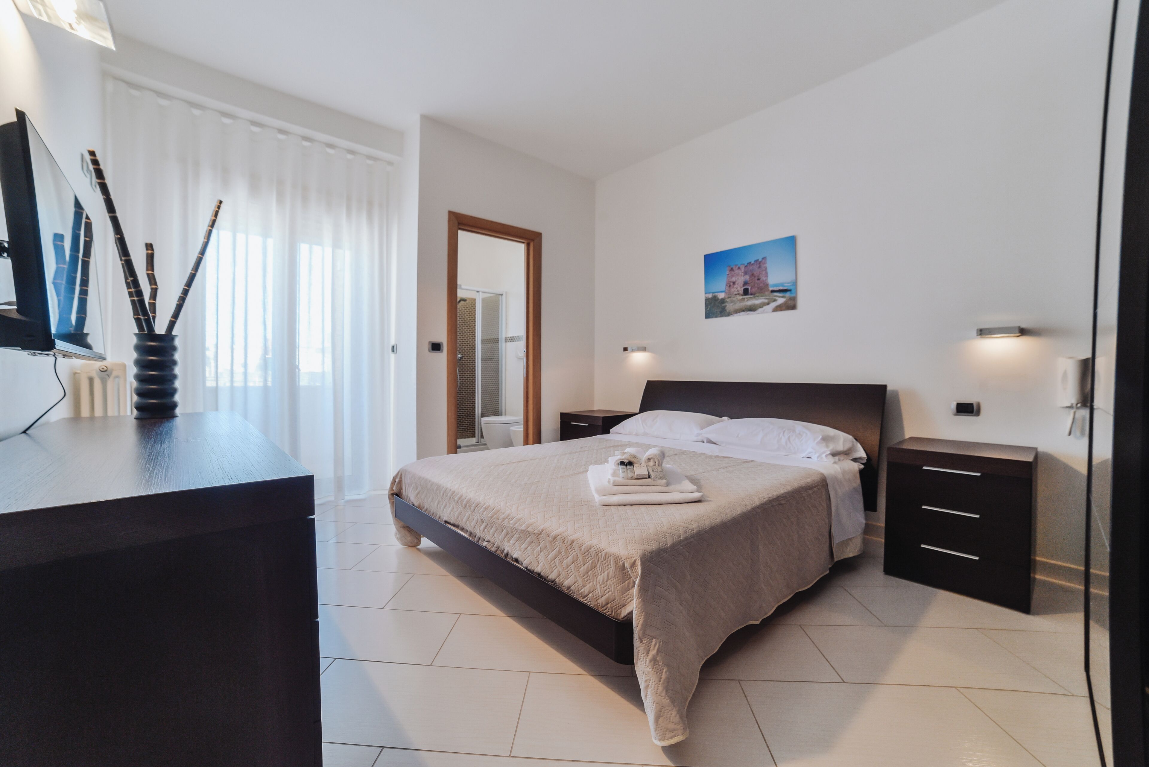 A modern bedroom with a large bed, bedside tables, a desk, and a window with curtains.