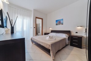 A modern bedroom with a large bed, bedside tables, a desk, and a window with curtains.