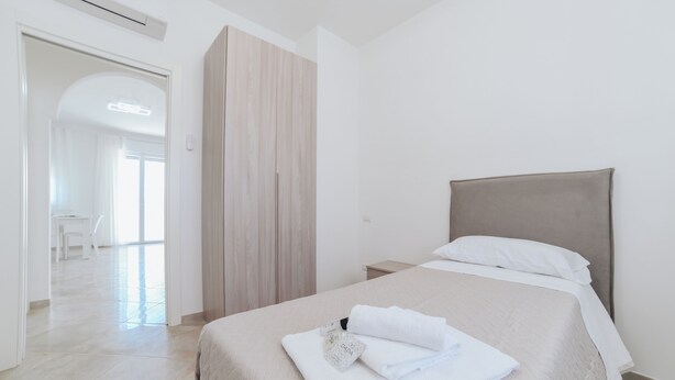 Habitación de hotel con cama, mesita de noche, armario y vista al pasillo.