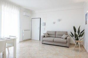 A modern living room with a white sofa, a dining table, and a radiator.