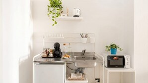 Una kitchenette compacta con un lavamanos, un microondas y una pequeña estantería con una planta y un hervidor.